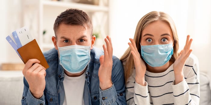 Global quarantine concept. Portrait of shocked couple in protective masks with canceled flight tickets