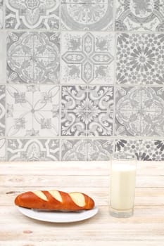 A rustic setting features freshly baked bread and a glass of milk, enhanced by a lovely tile background
