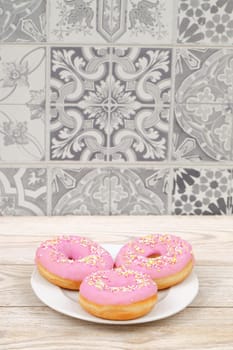 Three enticing pink donuts with colorful sprinkles, beautifully arranged against a decorative tile background