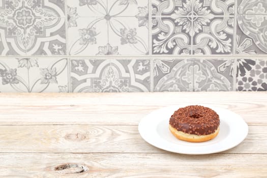 A tempting chocolate donut with colorful sprinkles sits on a white plate against a patterned background