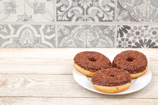 Three tempting chocolate donuts with colorful sprinkles on a white plate, perfect for dessert lovers. Enjoy