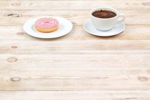 A delightful and charming coffee cup paired perfectly with a pink frosted donut, set on a rustic wooden table