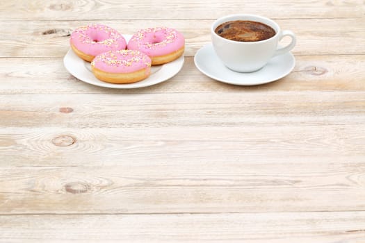 Enjoy a cozy and delightful moment with delicious pink donuts and a steaming cup of coffee on a rustic wooden table
