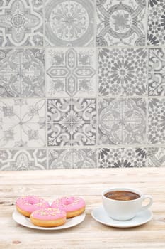Enjoy a cozy setting with delightful pink donuts paired with warm coffee against a beautifully patterned backdrop