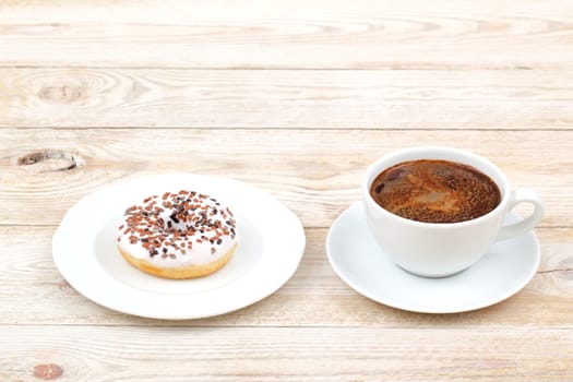 A delicious donut topped with chocolate sprinkles is sitting next to a steaming cup of coffee on a rustic wooden table
