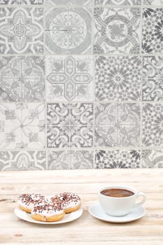 A stylish display of donuts and fresh coffee on a rustic wooden table with a patterned tile backdrop