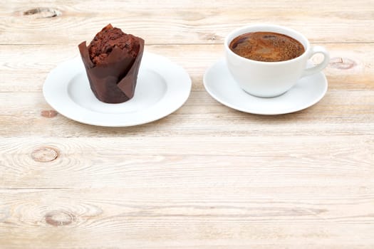 A deliciously rich chocolate muffin is served alongside a steaming cup of coffee on a rustic wooden table