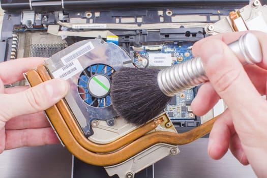 Man cleans the cooling system of the laptop cooler with a brush from the dust, close-up