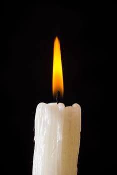 White candle burning with yellow fire on a black background