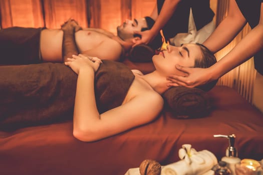 Couple customer enjoying relaxing anti-stress head massage and pampering facial beauty skin recreation leisure in warm candle lighting ambient salon spa in luxury resort or hotel. Quiescent
