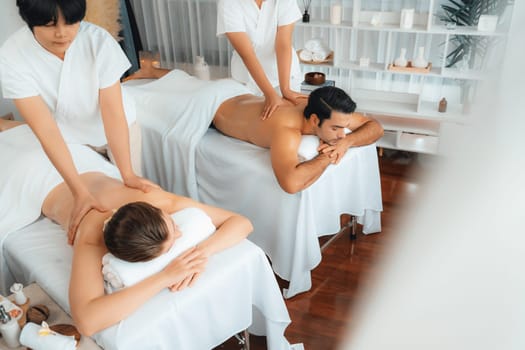 Caucasian couple customer enjoying relaxing anti-stress spa massage and pampering with beauty skin recreation leisure in day light ambient salon spa at luxury resort or hotel. Quiescent