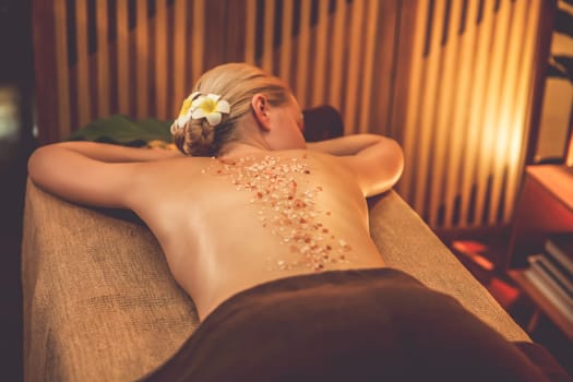 Woman customer having exfoliation treatment in luxury spa salon with warmth candle light ambient. Salt scrub beauty treatment in Health spa body scrub. Quiescent