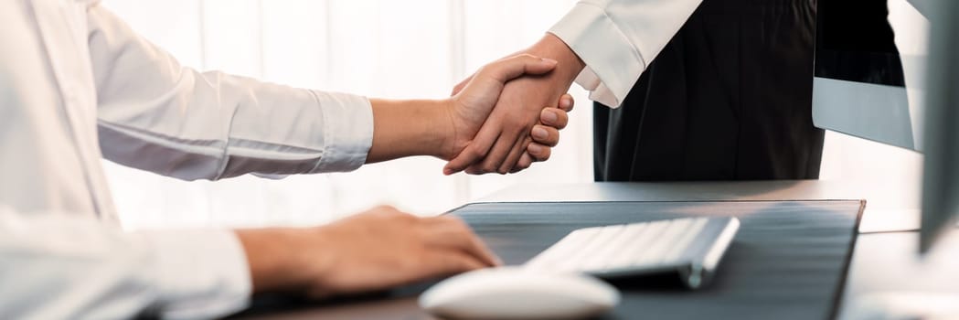 Office worker shake hand to colleague on workspace desk. Successful collaboration and cooperation between employee or coworker. Handshaking after success meeting with strong teamwork. Trailblazing