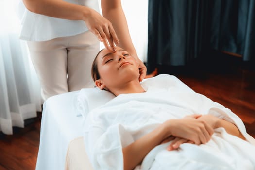 Caucasian woman enjoying relaxing anti-stress head massage and pampering facial beauty skin recreation leisure in dayspa modern light ambient at luxury resort or hotel spa salon. Quiescent