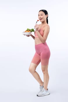 Young sporty Asian woman in sportswear holding salad bowl fill with vibrant of fruit and vegetable. Natural youthful and fit body lifestyle with balance nutrition on isolated background. Vigorous