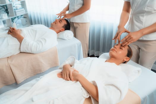 Caucasian couple enjoying relaxing anti-stress head massage and pampering facial beauty skin recreation leisure in dayspa modern light ambient at luxury resort or hotel spa salon. Quiescent