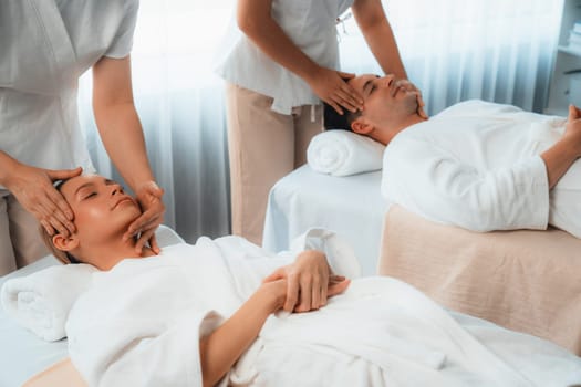 Caucasian couple enjoying relaxing anti-stress head massage and pampering facial beauty skin recreation leisure in dayspa modern light ambient at luxury resort or hotel spa salon. Quiescent