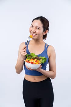 Young sporty Asian woman in sportswear holding salad bowl fill with vibrant of fruit and vegetable. Natural youthful and fit body lifestyle with balance nutrition on isolated background. Vigorous