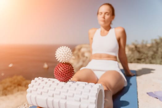 Middle aged well looking woman with black hair doing Pilates with the ring on the yoga mat near the sea on the pebble beach. Female fitness yoga concept. Healthy lifestyle, harmony and meditation.