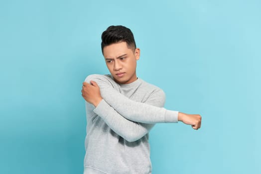 young asian man gesture pain his shoulder or arm in pain isolated on blue background