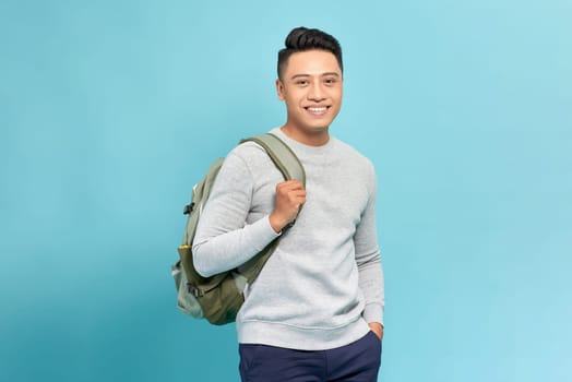 Smiling happy young Asian man in casual clothes backpack standing isolated on blue background.