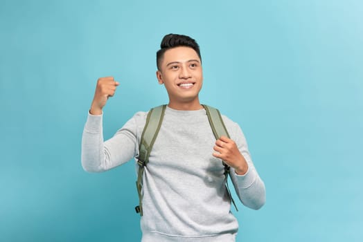 Portrait of happy excited young Asian tourist backpacker man raising his fists doing success gesture