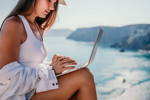 Digital nomad, Business woman working on laptop by the sea. Pretty lady typing on computer by the sea at sunset, makes a business transaction online from a distance. Freelance remote work on vacation