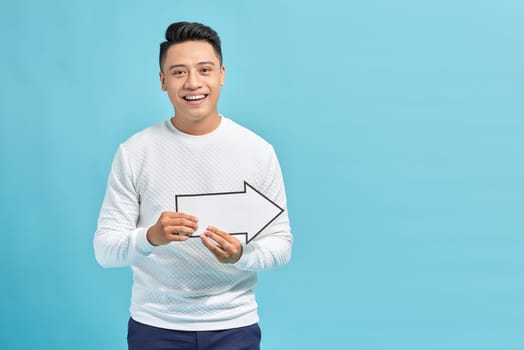 Good looking young man holding a white arrow, isolated on a blue background