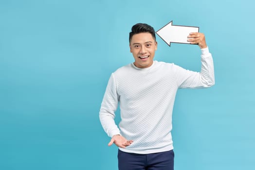 Good looking young man holding a white arrow, isolated on a blue background
