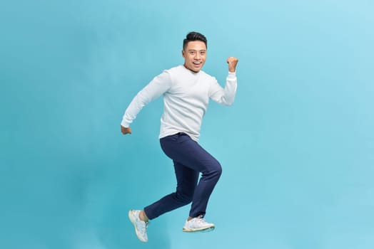 Photo of emotional excited young man jumping isolated on blue