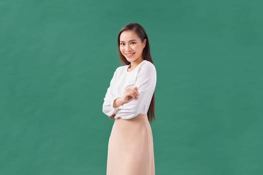 Beautiful girl with folded arms looking at camera against green wall. 