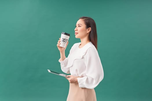 young woman holding digital tablet and paper cup isolated on green