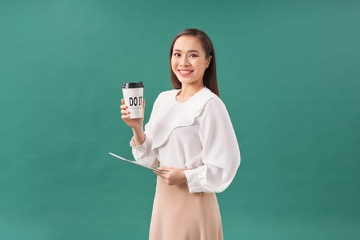 young woman holding digital tablet and paper cup isolated on green