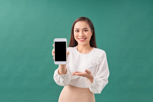 portrait of a smiling asian woman showing blank screen mobile phone isolated over green background