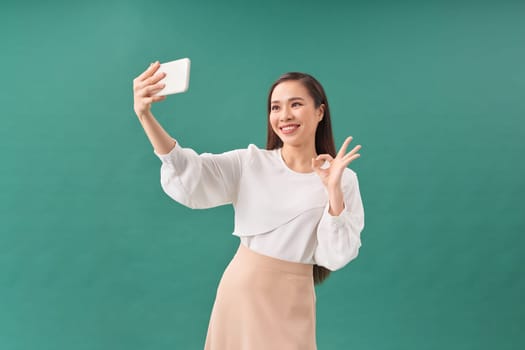 Portrait of pretty cheerful girl in casual clothes smiling and taking selfie using mobile phone