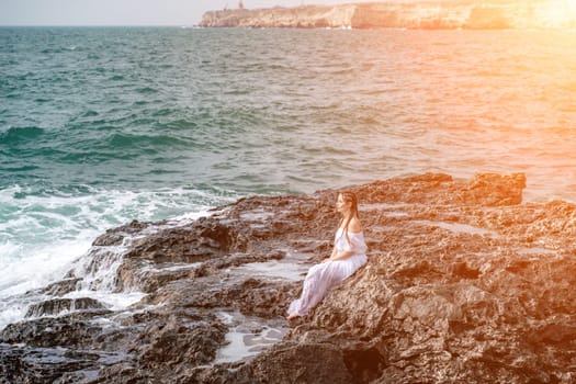 A woman in a storm sits on a stone in the sea. Dressed in a white long dress, waves crash against the rocks and white spray rises