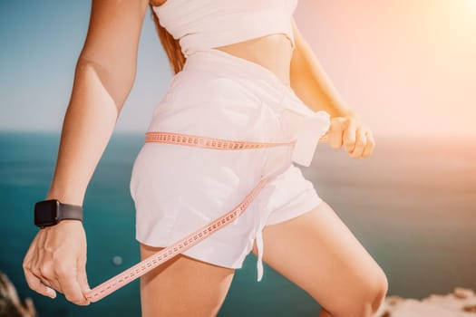 a young and slender woman in shorts holds in her hand a measuring yellow tape on her sexy thighs on the beach. concept of detox and diet