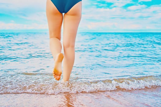 In the frame of a woman's feet walking on the beach by the sea on a Sunny day in a tropical hotel on vacation. Waves of ocean wash her feet