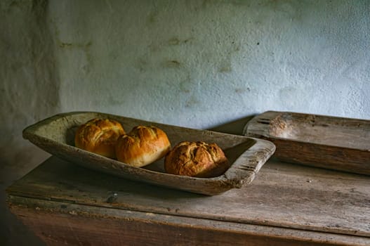 Old-fashioned bread loaves rest in a vintage wooden trough, evoking a sense of rustic simplicity and traditional baking. The scene captures the charm of handcrafted food and historic kitchen decor.