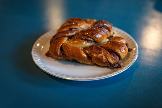 A close-up of a freshly baked cinnamon pastry served on a white plate. The warm, inviting lighting enhances its golden-brown texture, creating a cozy and appetizing atmosphere in denmark