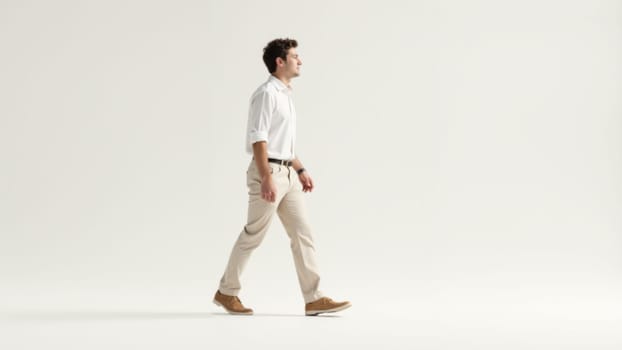 A confident man strides across a clean, minimalist backdrop, highlighting his stylish outfit and relaxed demeanor in soft, natural light, evoking a sense of calm and self-assuredness.