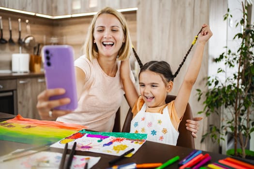 A joyful mother and her daughter capture a delightful moment together as they create beautiful art in their home