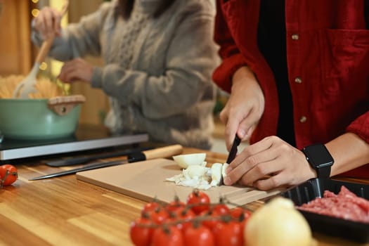Man slicing onions on a cutting board for homemade pasta dish during the holiday season.