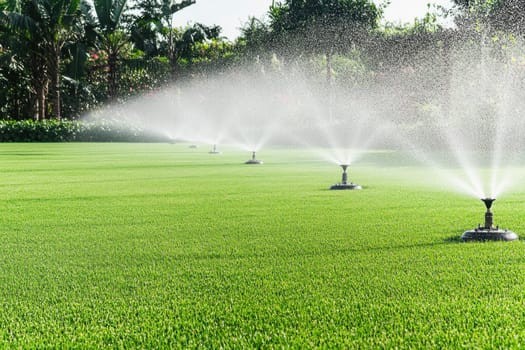Water sprinklers irrigating green grass field on a golf course or sports field