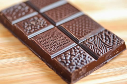Bar of dark chocolate featuring a variety of textures and patterns sits on a wooden cutting board
