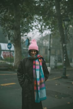A woman adorned in a charming pink hat and a stylish scarf is standing elegantly on a bustling street, enjoying the city life