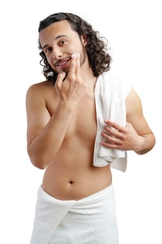 A young man applies skincare product on his face in a minimalist setting close up