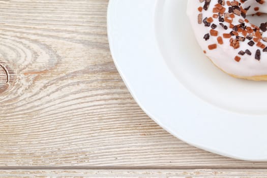 A beautifully crafted closeup of a frosted doughnut topped with colorful sprinkles resting on a vintage wooden table