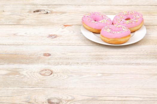 These delicious pink frosted donuts, adorned with colorful sprinkles, are perfect for dessert on a white plate