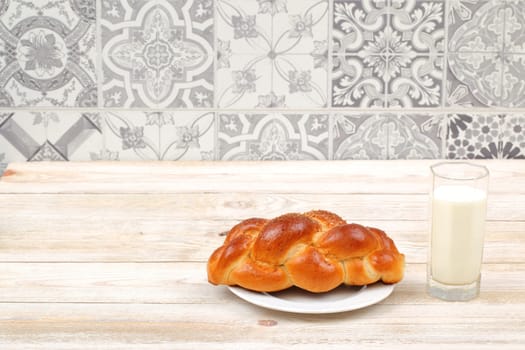 A delightful and delicious challah bread served warm, accompanied by a refreshing glass of cold milk on a rustic table